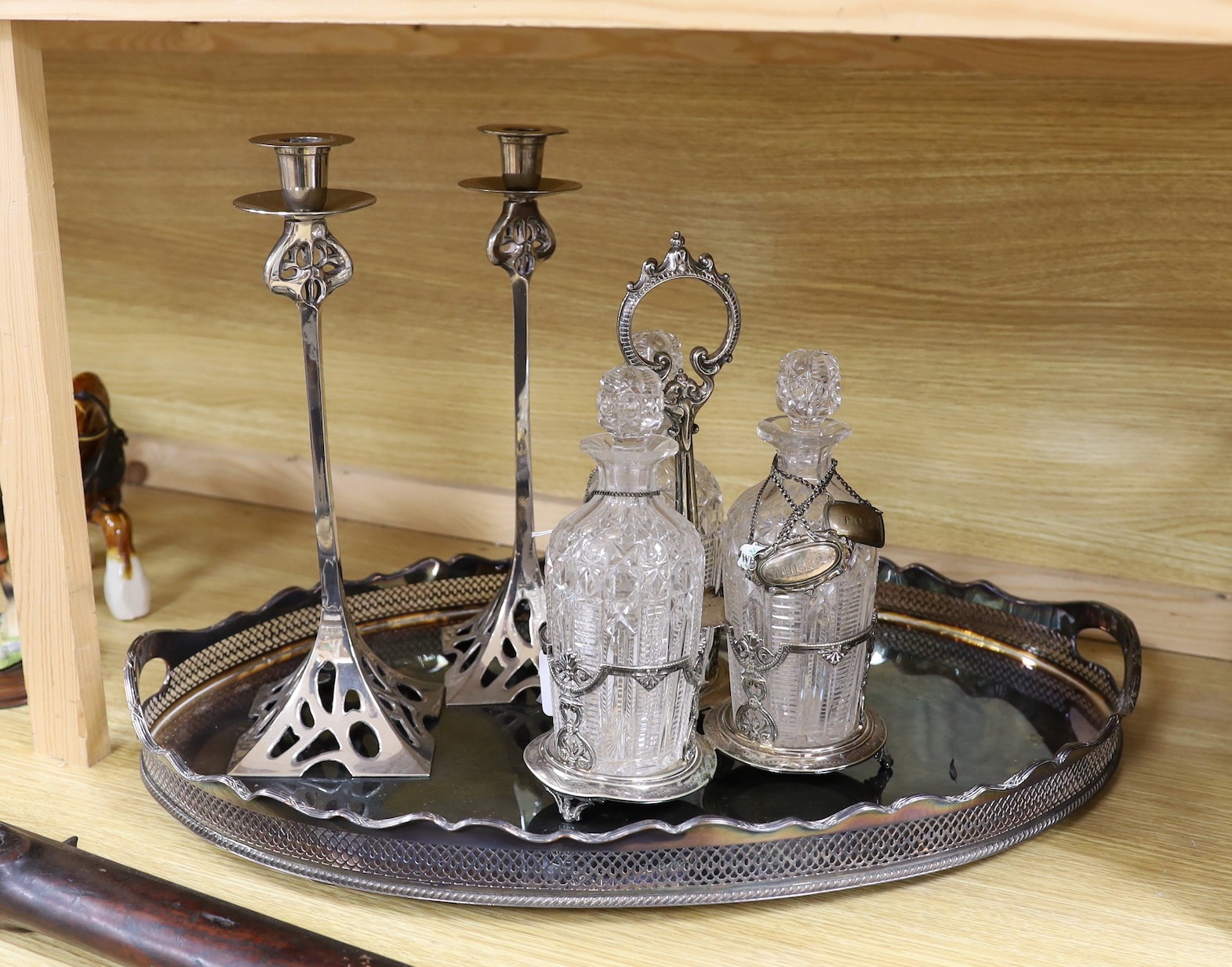 An oval silver plated tray, a three bottled tantalus and a pair of candlesticks, a silver ‘Whiskey’ label, two enamelled silver labels ‘Gin’ and ‘Whisky’ and two plated labels
